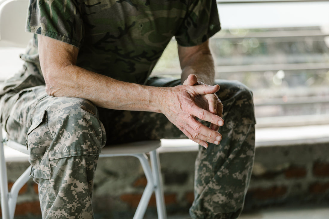 Older service member in camouflage uniform seated with hands clasped, awaiting a medical assessment