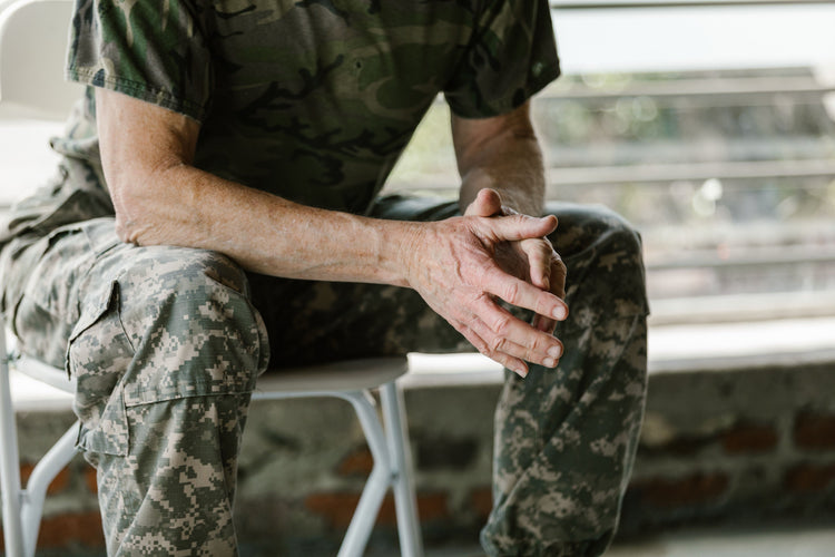 Older service member in camouflage uniform seated with hands clasped, awaiting a medical assessment