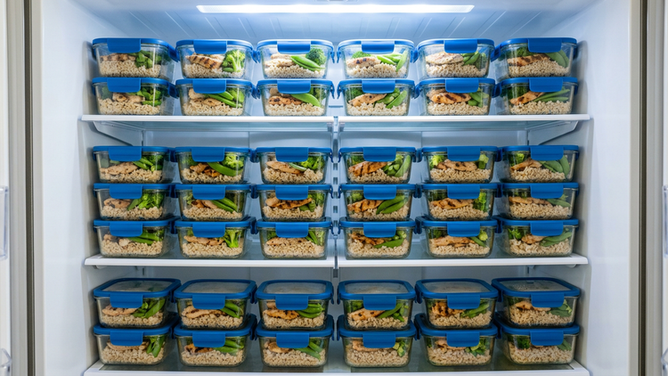 Refrigerator shelves filled with rows of identical meal prep containers of chicken, rice and broccoli
