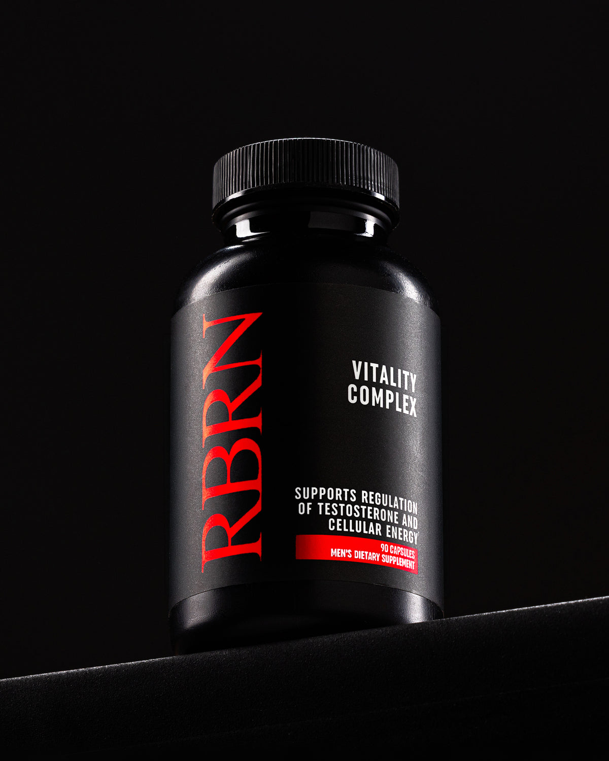 RBRN Vitality Complex bottle standing on a black ledge in a dark studio